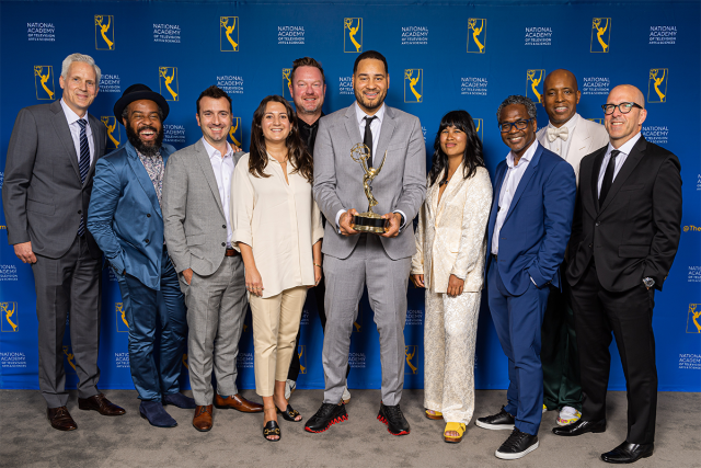 Erik Parker, holding the Emmy Award, stands in the center of a group of people.