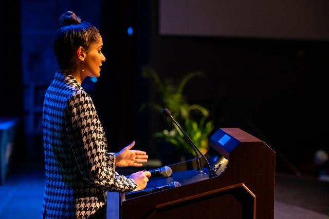 Side profile image of Sophia Kianni on stage speaking behind the podium