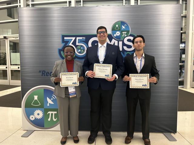 Three students, one female, two male holding certificates for their wins in a research competition