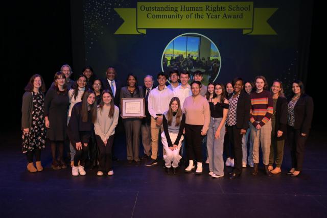 A group of high school students and staff from the "Outstanding Human Rights School Community Award of the Year" recipient and President Repollet on stage for a group picture