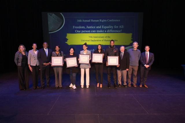 A group of faculty, President Repollet, and the speakers on stage, lined up next to each other for a group picture