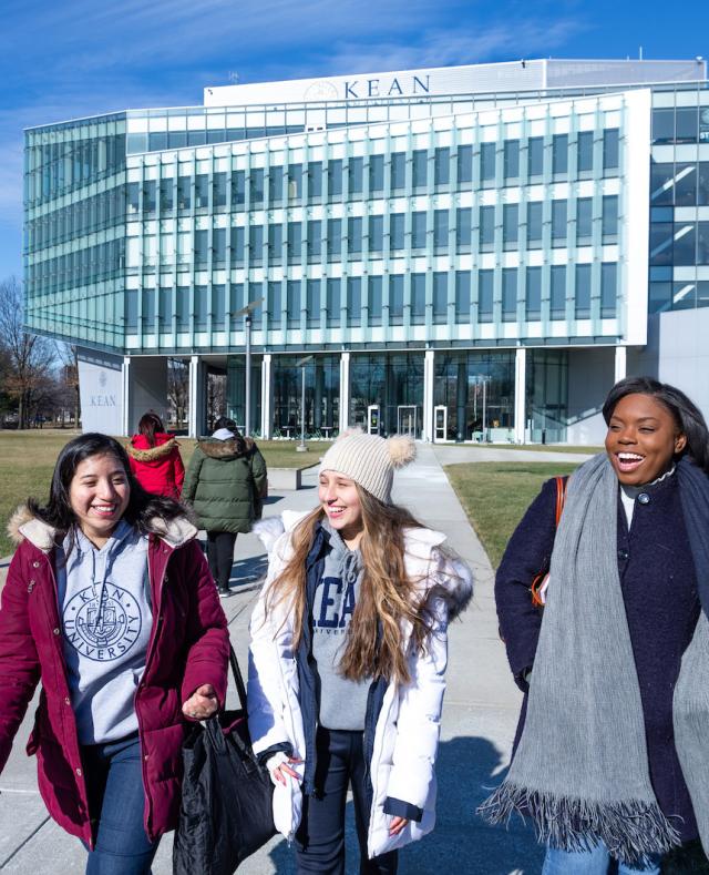 Three students walking in cold weather outfits with a Kean building in the background