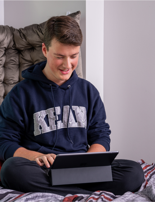 Student seated cross-legged on bed, working on a laptop