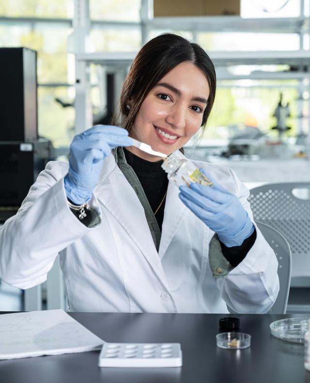 Researcher in lab coat and gloves holding a vial and pipette
