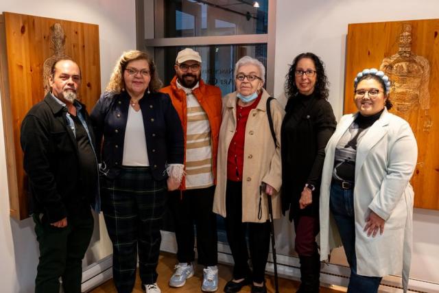 Four women, two men wearing colorful clothing standing in front of artwork side by side posing for the camera