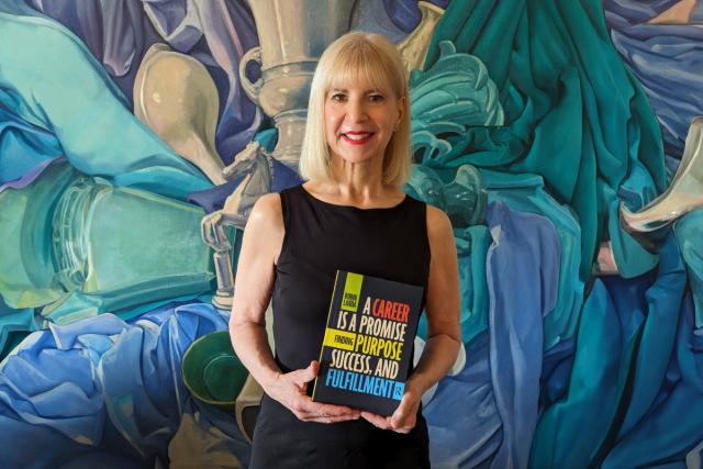 Robin Landa stands in front of a colorful background holding her book