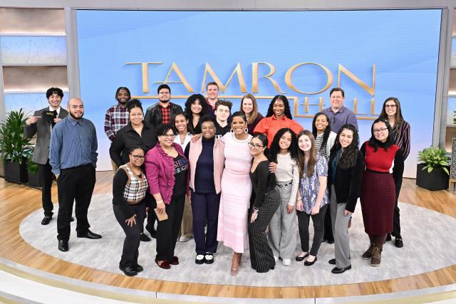 Group of students of diverse backgrounds standing with beside a woman in a pink dress, heels, short hair