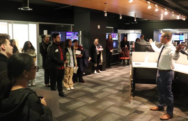 A group of students and a speaker in a facility discussing the behind the scenes