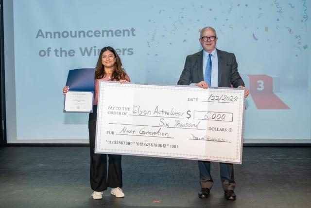 The winner of the Business Plan Competition, Joceline Guerra, stands with Kean's provost holding a big check for $6,000.