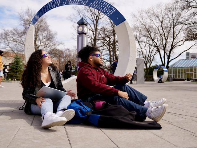 Male and female sitting on the ground with solar eclipse glasses on looking up at the sky 