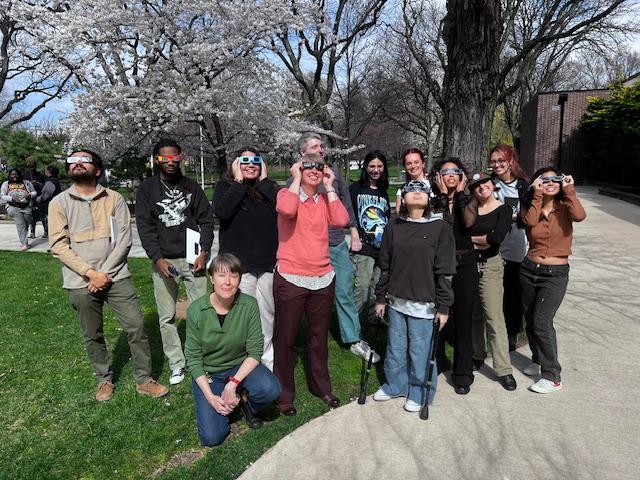 Group of students and teachers with diverse backgrounds holding the eclipse glasses looking up outside on campus