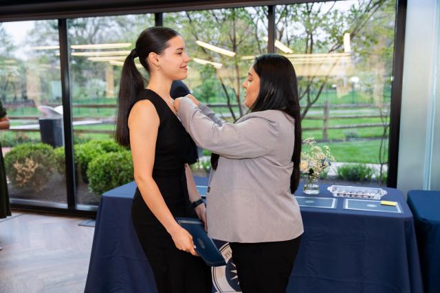 A female student receives an honor society pin from a family member.