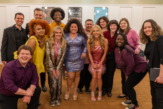 A diverse group of young men and women standing close to 3 adult women in sparkly outfits in the center