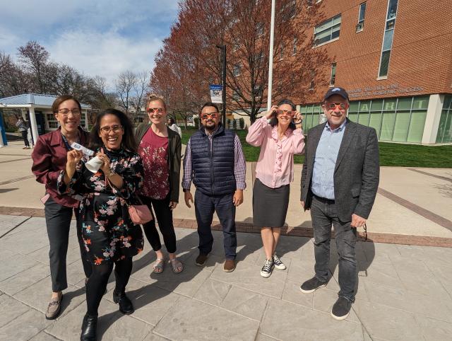 Group of professors of diverse backgrounds outside wearing eclipse glasses