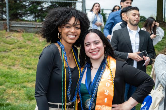 Two girls of diverse background, curly hair, and straight hair wearing colorful stoles 