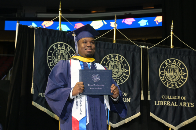 A male student on stage at Kean University's Undergraduate Commencement after receiving his diploma cover.
