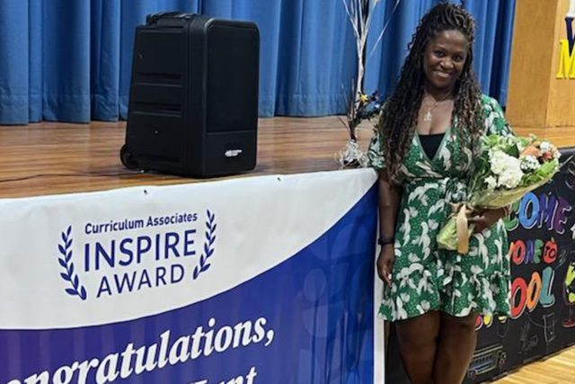 Tomeeko Hunt, a Black woman in a green floral dress, smiles as she stands next to an Inspire Awards Congratulations banner.