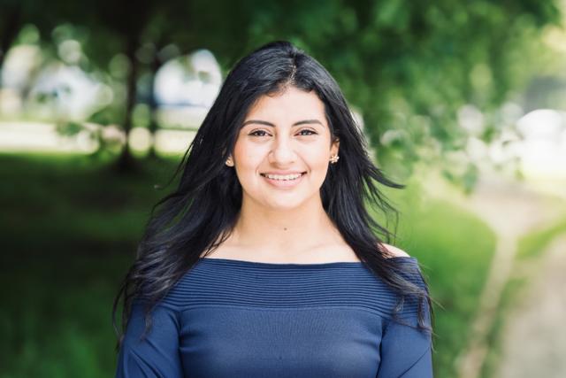 Diana Calle, with long dark hair and wearing a blue shirt, poses outdoors with trees behind her.