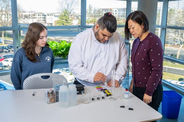 Female faculty researcher and female student researcher look on as a male student conducts research.