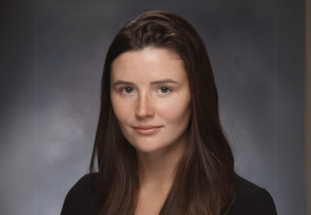 Headshot of white female with brown hair, back top; gray background