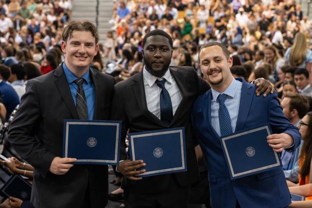 Three male students show off honors certificates