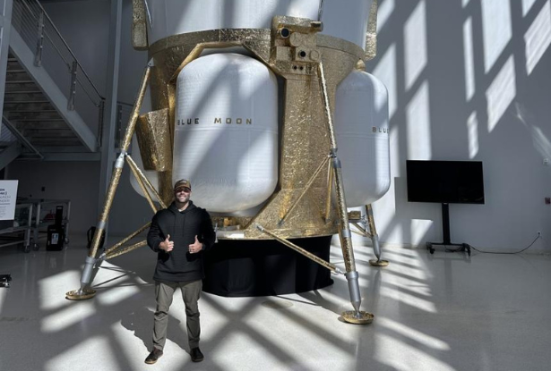 Male standing in front of a very large white and brown machine in a sunlit room.