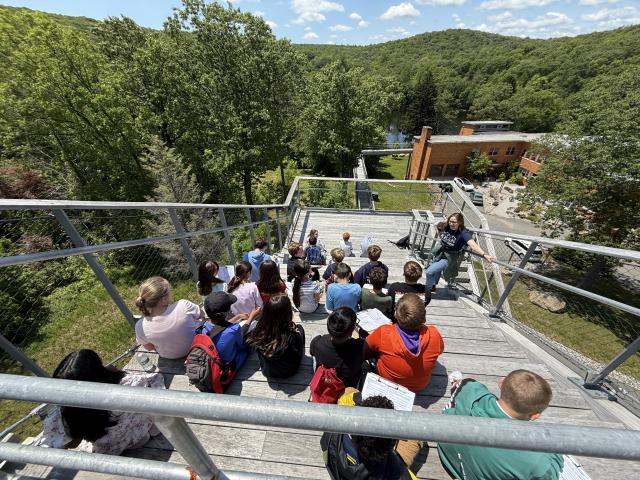 Group of students sitting on Skywalk looking over the campus with a Kean professional, learning about things seen in nature.