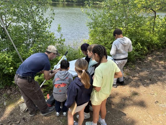 Group of students by a lake being taught by a Kean professional regarding organisms in the lake.