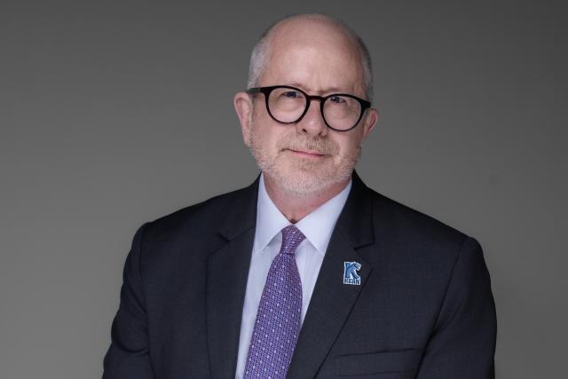 White male with glasses in suit jacket with purple tie