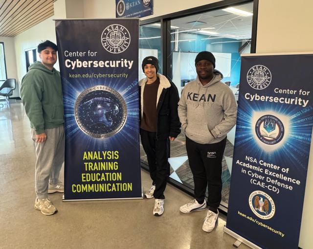 Three students in Kean's NPCIR cybersecurity program in front of banners