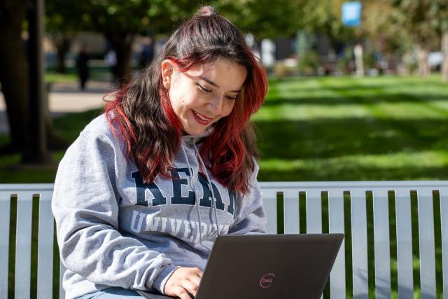 Student Sitting on a Bench and looking at Laptop