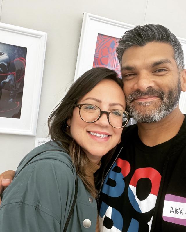 woman with dark hair and glasses posing with her husband, a male with salt and pepper hair and short beard