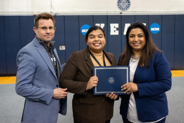 Woman holding an award standing next to another woman and a man