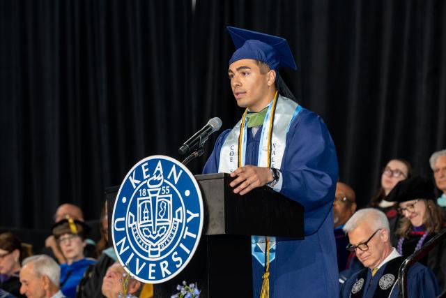 Man in graduation attire speaking at a podium