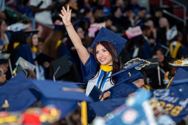 Woman in graduation cap and gown waving