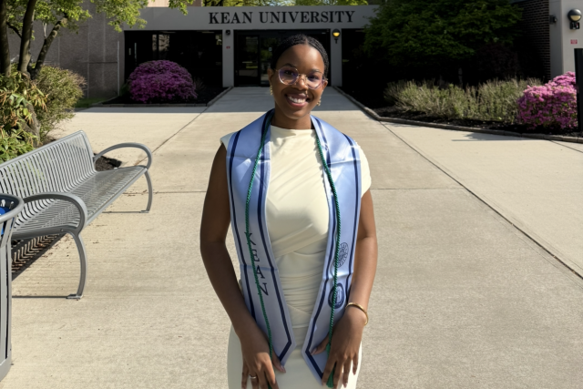 Woman in graduation attire standing in front of building at Kean