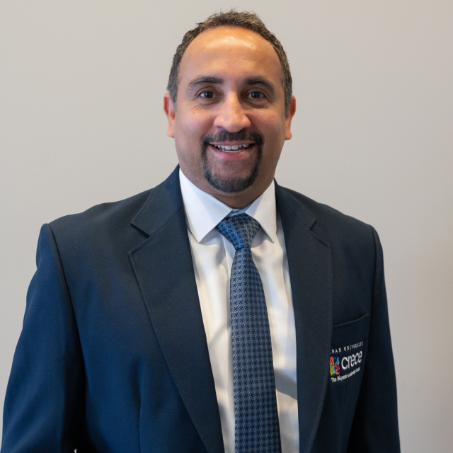 Smiling Hispanic male wearing a white shirt, blue tie and dark blue CRECE jacket