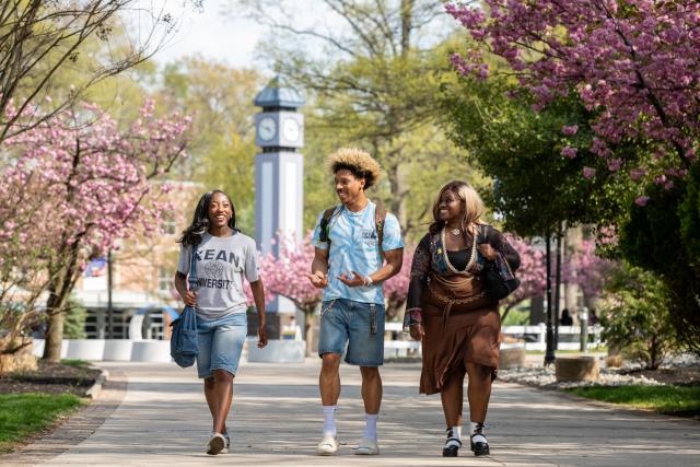 Three students walking on a sidewalk surrounded by trees