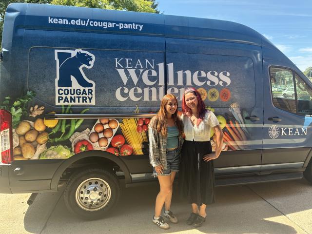 Two female students standing in front of a Kean Wellness Center van