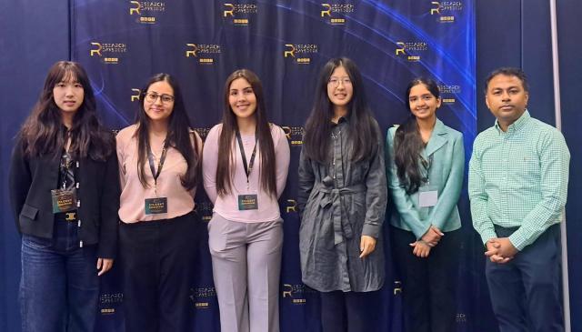 Five female students and one male professor in front of a blue backdrop