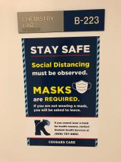 Photo of Pandemic sign outside of Chemistry Lab  saying masks are required and social distancing must be observed