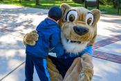 The Kean cougar mascot bends down to hug a little boy.