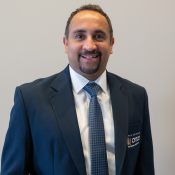 Smiling Hispanic male wearing a white shirt, blue tie and dark blue CRECE jacket