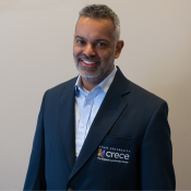 Smiling Hispanic male wearing a light blue shirt and dark blue CRECE jacket